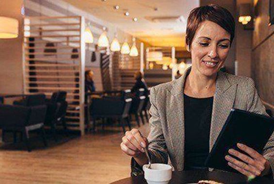 Woman drinking coffee whilst on tablet in lounge